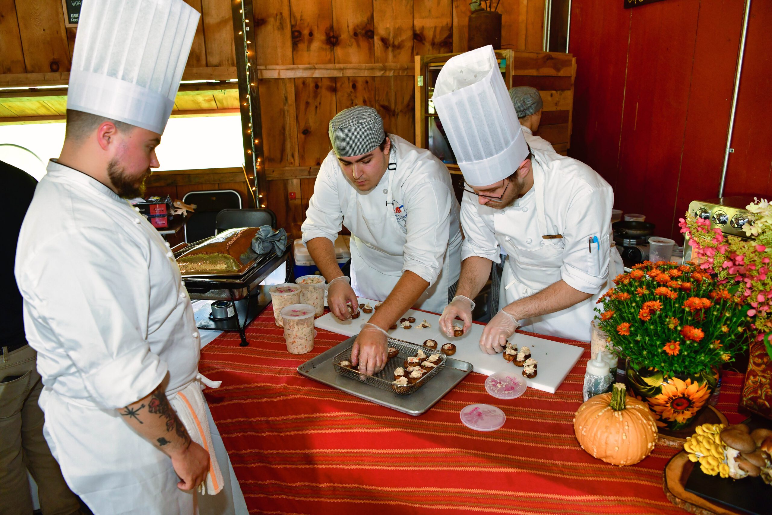 A chef watching two other chefs place h'orderves on a serving platter