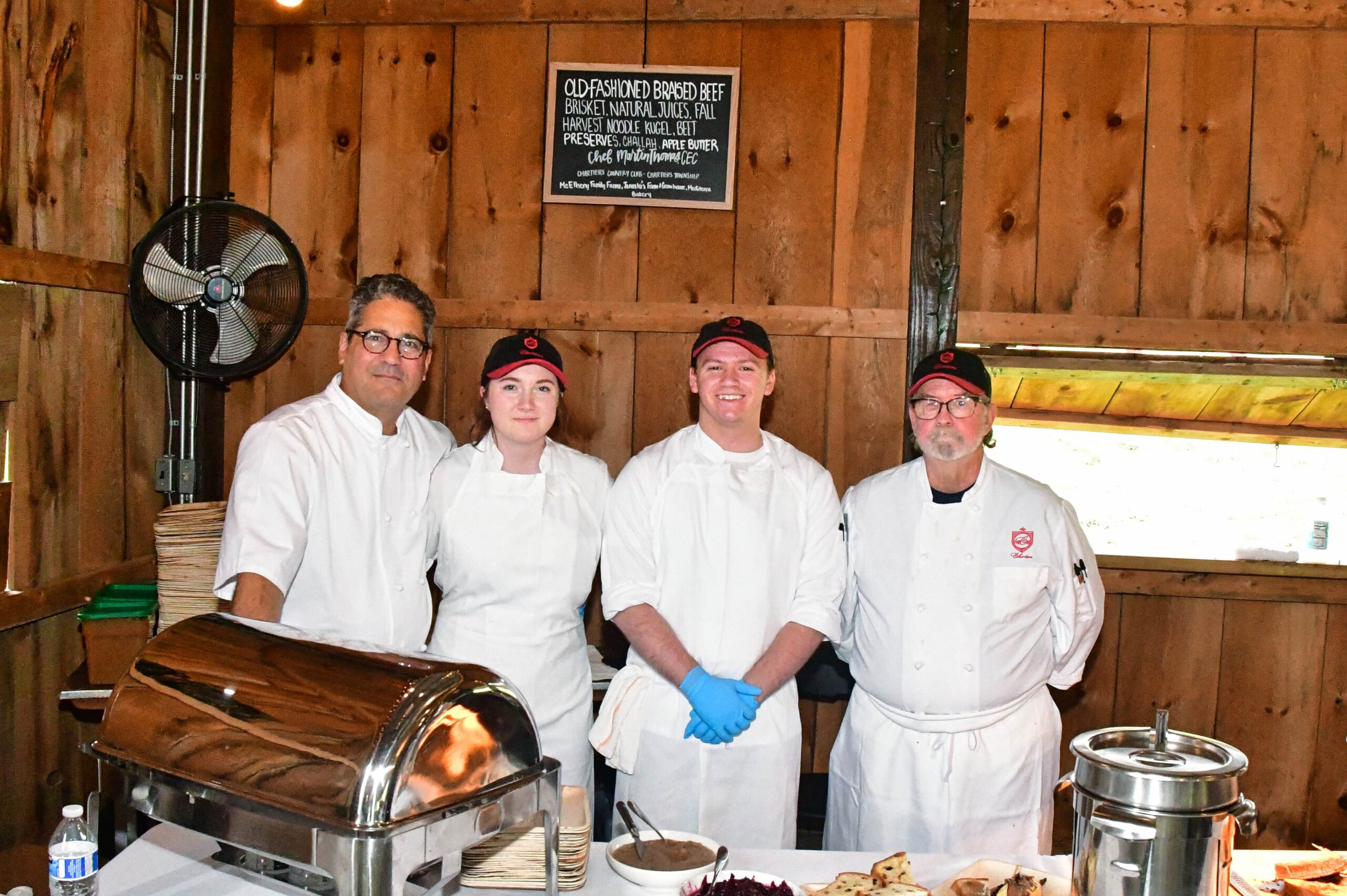 Four smiling chefs standing behind a table of food they will serve at an event