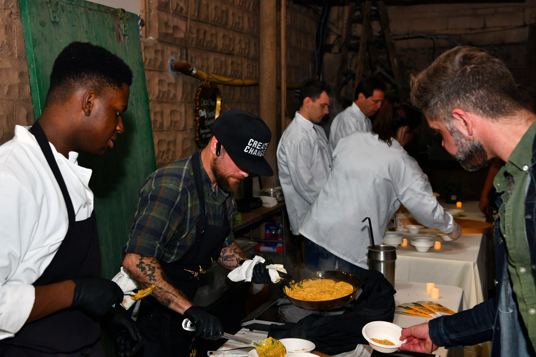 Chefs prepare and serve dishes at a live cooking station, engaging guests in a rustic industrial setting.