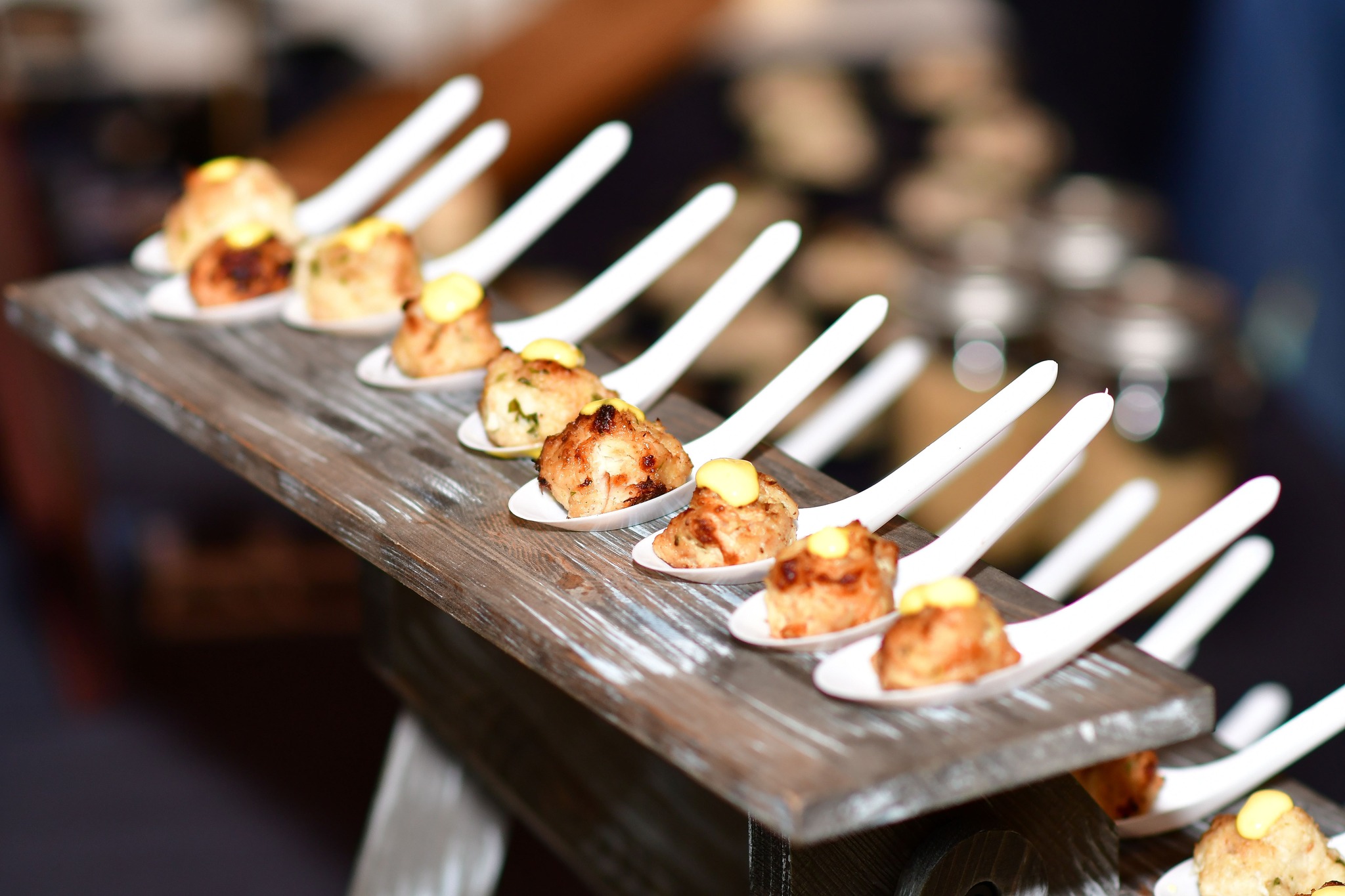 Close-up of bite-sized appetizers served on individual spoons, artfully arranged on a rustic wooden stand.