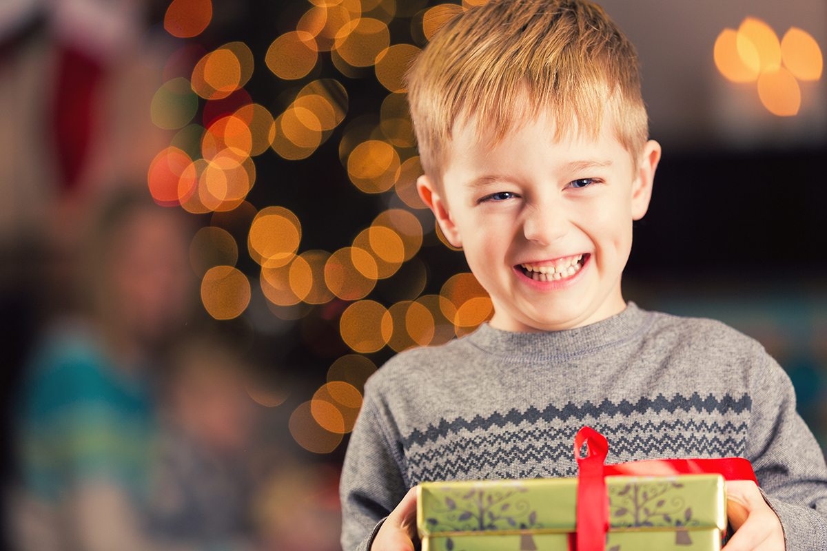 Excited young boy holding Christmas gift in front of tree